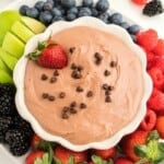 A white bowl of chocolate fruit dip topped with chocolate chips and a strawberry.