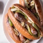 Three brats with toppings on a white plate.