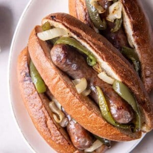 Three brats with toppings on a white plate.