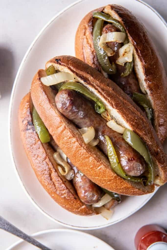 Three brats with toppings on a white plate.