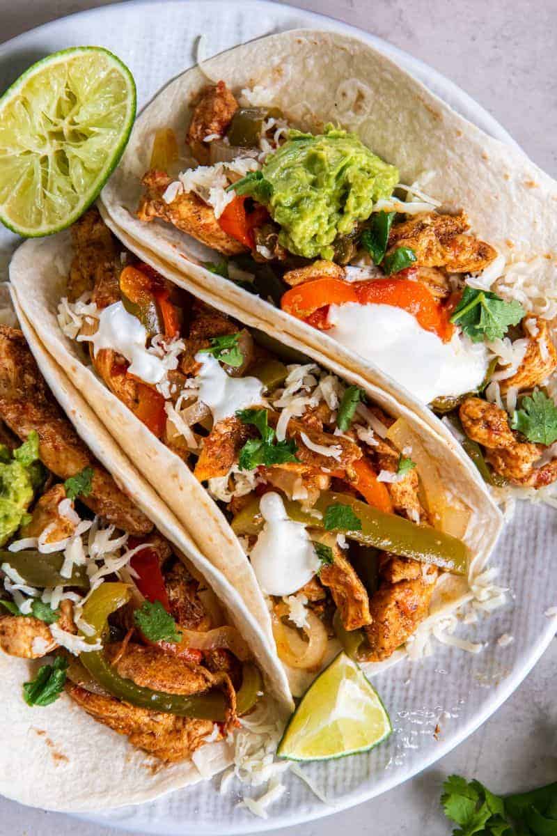 Three chicken fajitas on a white plate.