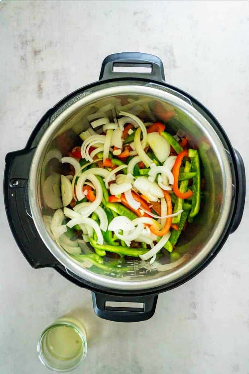 Adding salsa, onions and peppers to the seasoned chicken in the bottom of an Instant Pot.