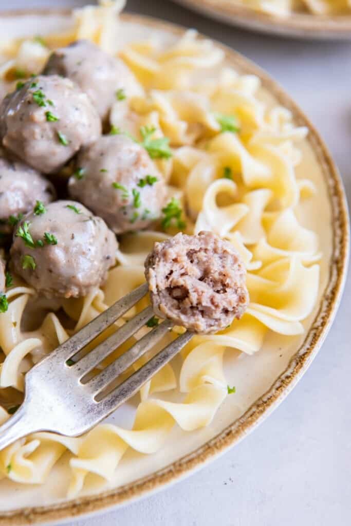 A fork holding a meatball with a bite taken out of it.