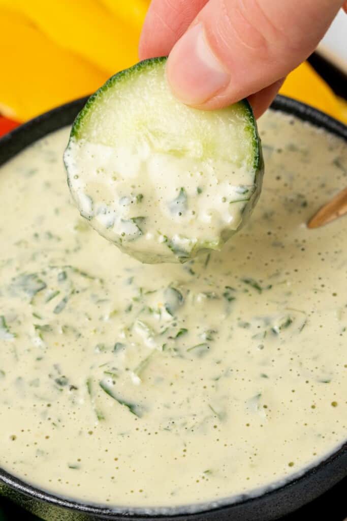 A slice of zucchini dipped into a bowl of lemon herb tahini.