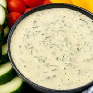 A bowl of lemon herb tahini surrounded by fresh vegetables.