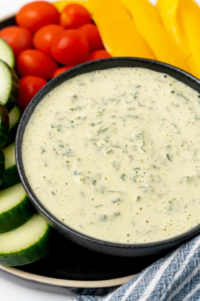 A bowl of lemon herb tahini surrounded by fresh vegetables.