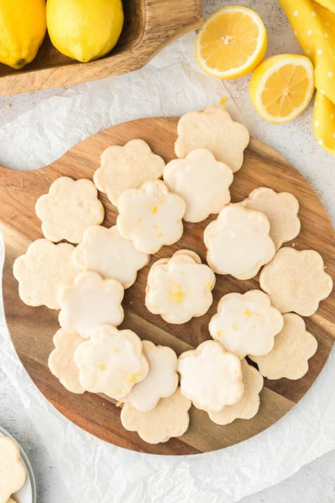 A batch of glazed lemon shortbread cookies on a wooden serving platter.