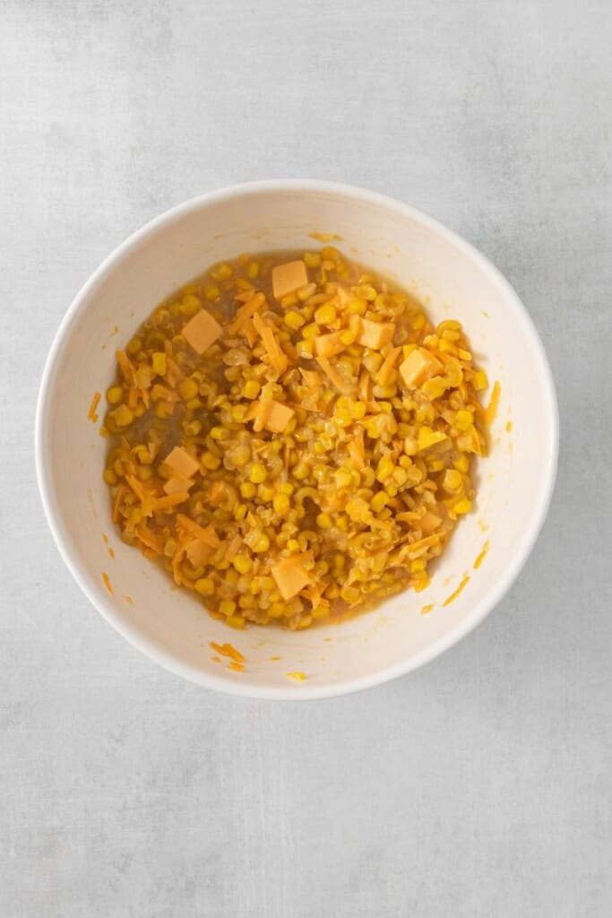 Combining ingredients for corn macaroni casserole in a white mixing bowl.
