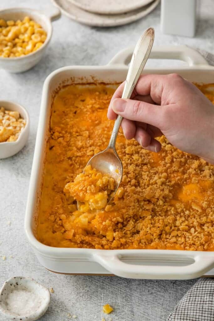 Spoon lifting a bite of corn macaroni casserole from the baking dish.