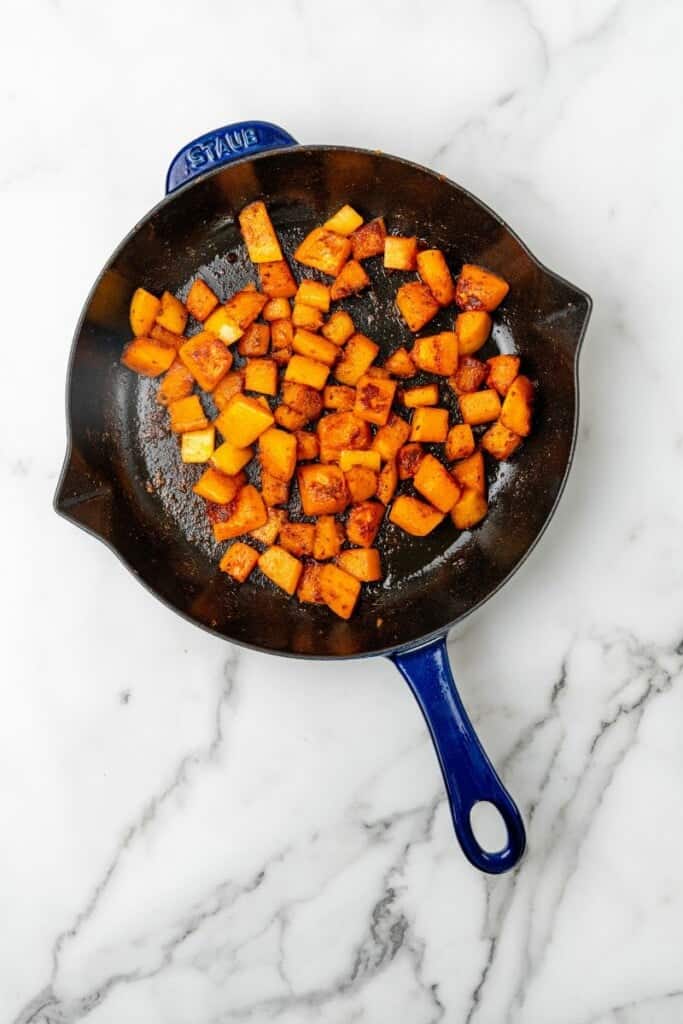 Seasoning added to diced butternut squash in a skillet.