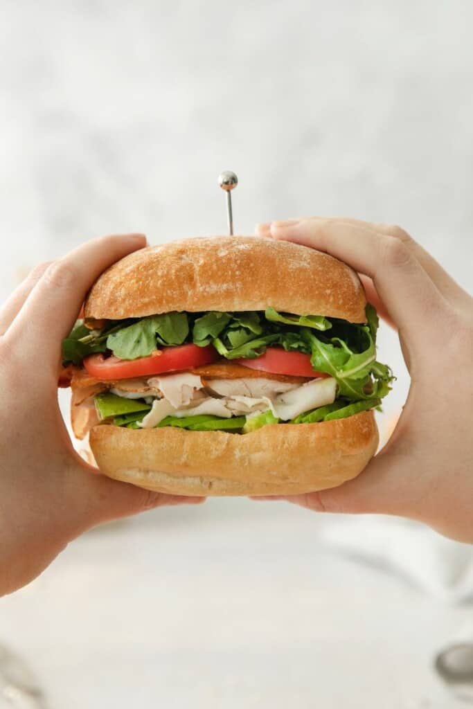 Two hands holding a turkey bacon avocado sandwich.
