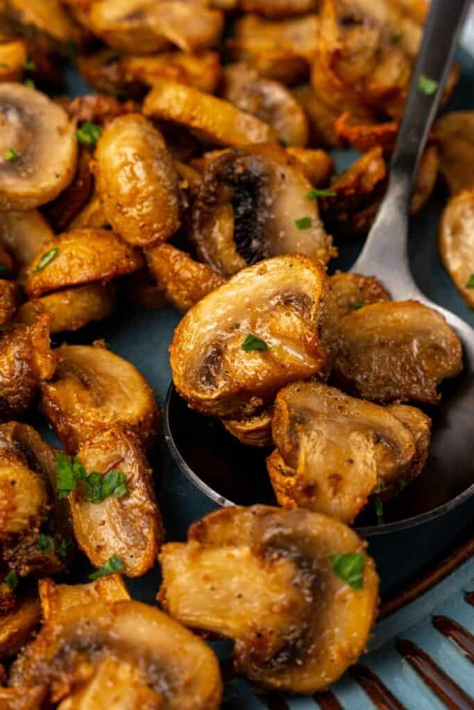 Close up of air fried mushrooms on a serving plate with a serving spoon.