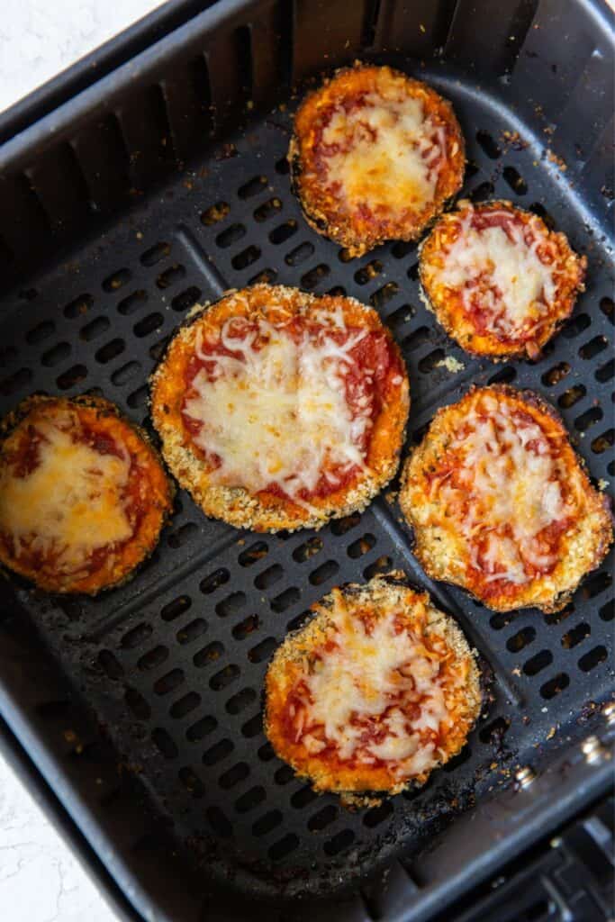 Cooked eggplant parmesan in an air fryer basket with the marinara and melted cheese on top.