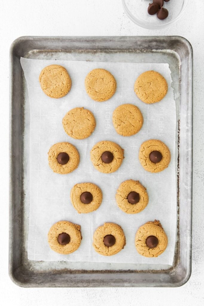 Easy peanut butter blossoms fully baked on a cookie sheet with half of them topped with one Hershey kiss each.