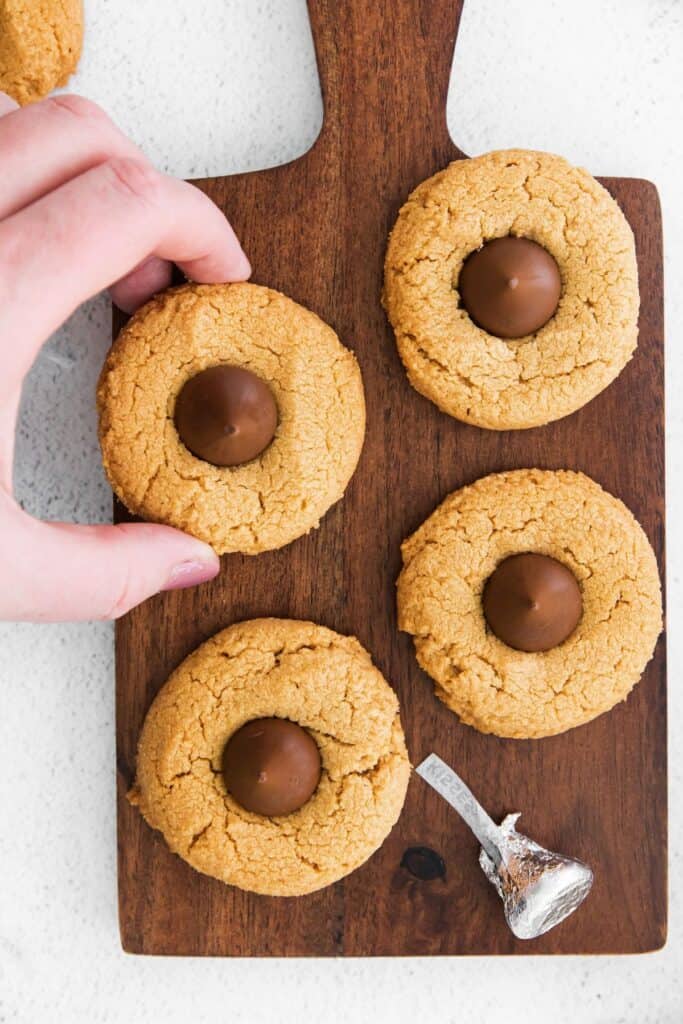 Peanut butter blossoms cookies on a serving board with a hand taking one of them off.