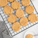 Baked peanut butter cookies on a cooling rack with a spoon holding a bite of peanut butter.