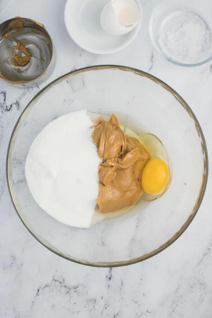 Combining the three ingredients for peanut butter cookies in a clear mixing bowl.