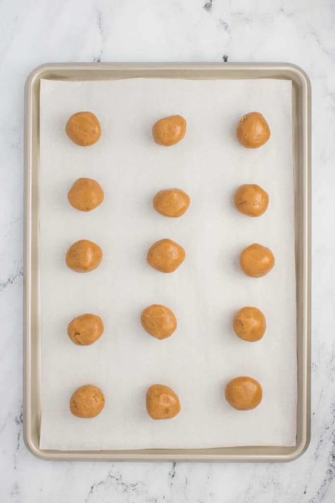 Scoops of peanut butter cookie dough on a parchment lined baking sheet.