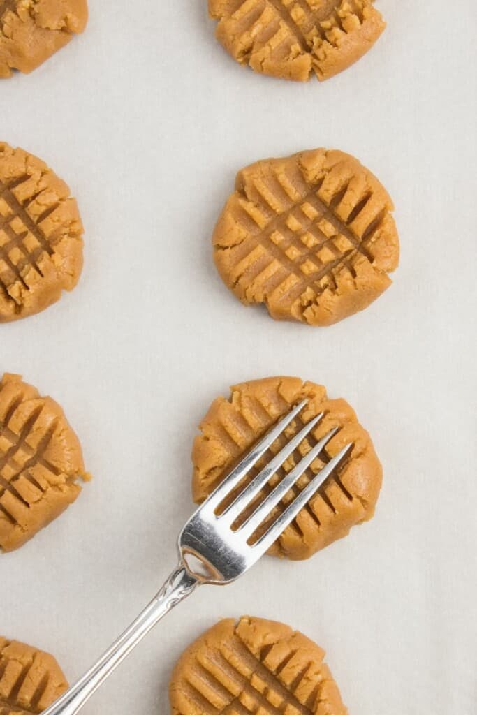 Using a fork to flatten peanut butter cookie dough and make criss cross pattern on the top.