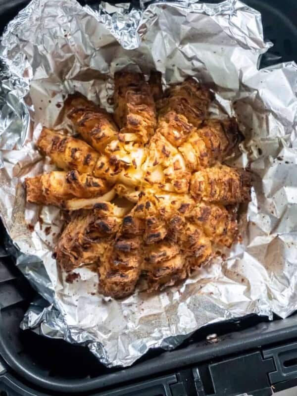 Closeup view of a prepared blooming onion on aluminum foil in a black air fryer basket.