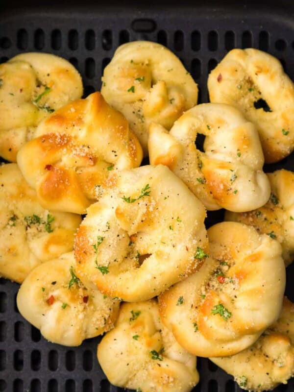 Close up view of prepared garlic knots with seasoning resting in a black air fryer basket.
