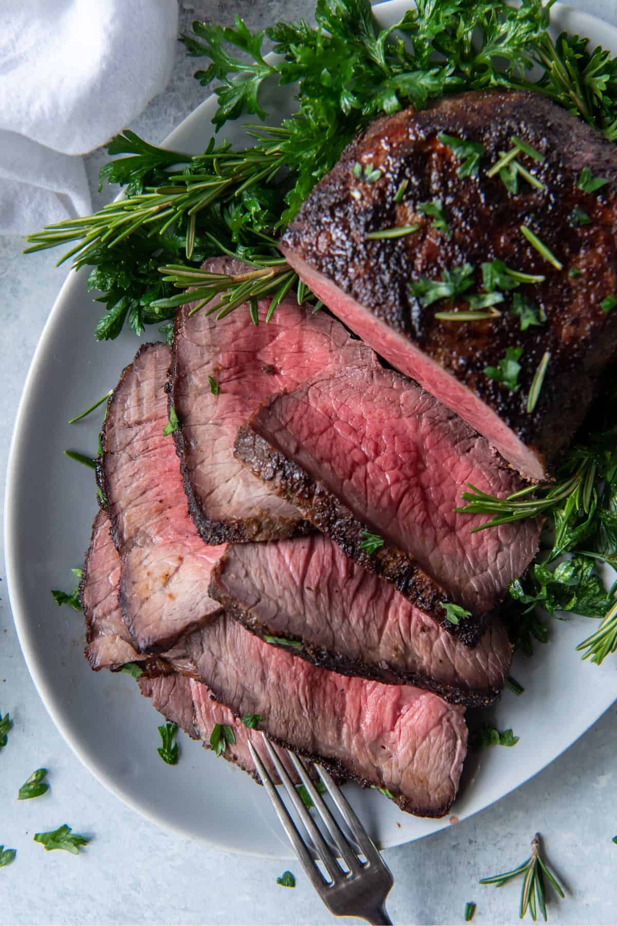 Overhead view of air fryer roast beef half sliced on a serving plate.