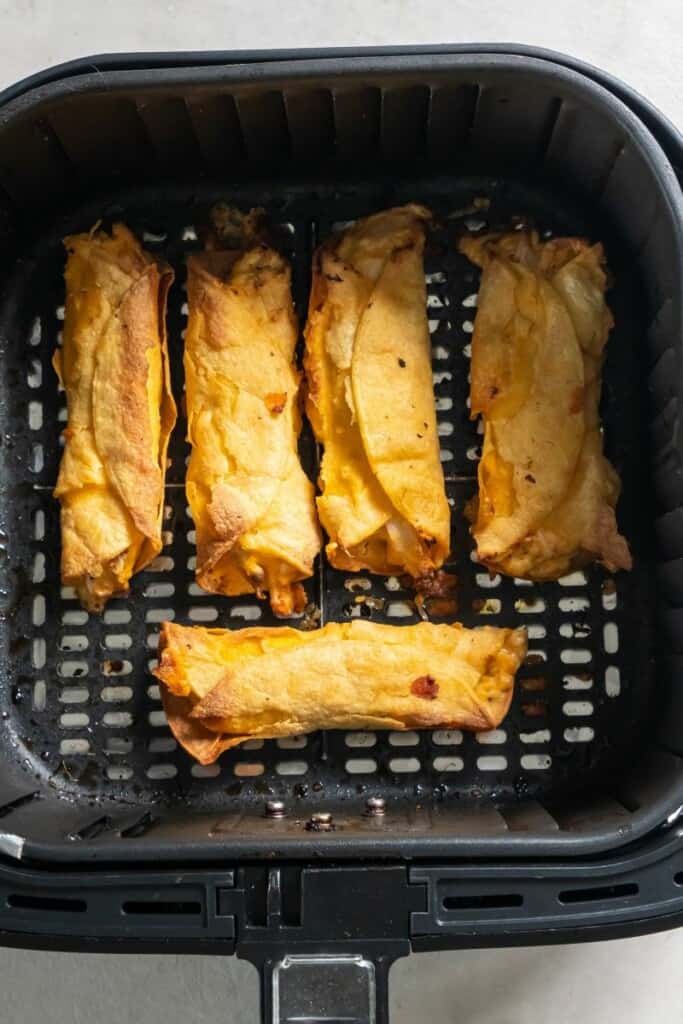 Five cooked taquitos resting in a black air fryer basket.
