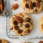 A few chocolate chip cookies with pecans on a cooling rack.