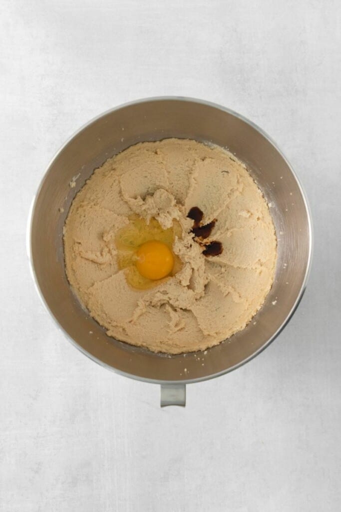 Adding egg and vanilla extract to mixing bowl of combined butter and brown sugar.