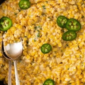 Jalapeno cream corn topped with additional jalapeno slices in a cast iron skillet with a spoon.