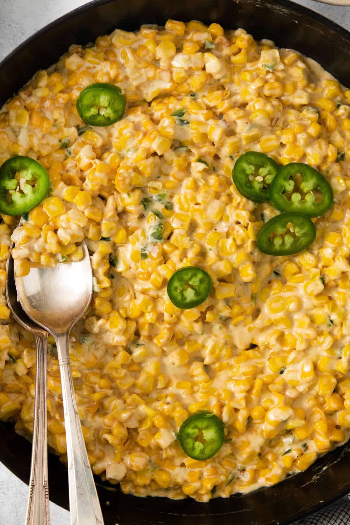 Jalapeno cream corn topped with additional jalapeno slices in a cast iron skillet with a spoon.