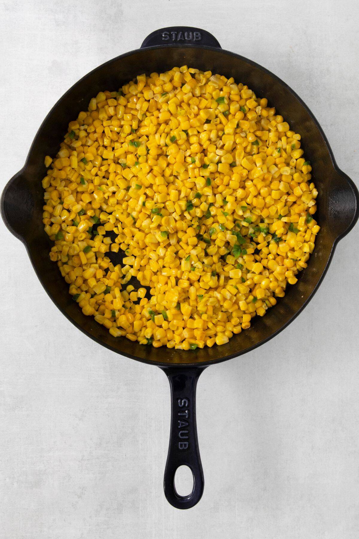 Corn being cooked in a cast iron skillet with butter, jalapenos, and salt.