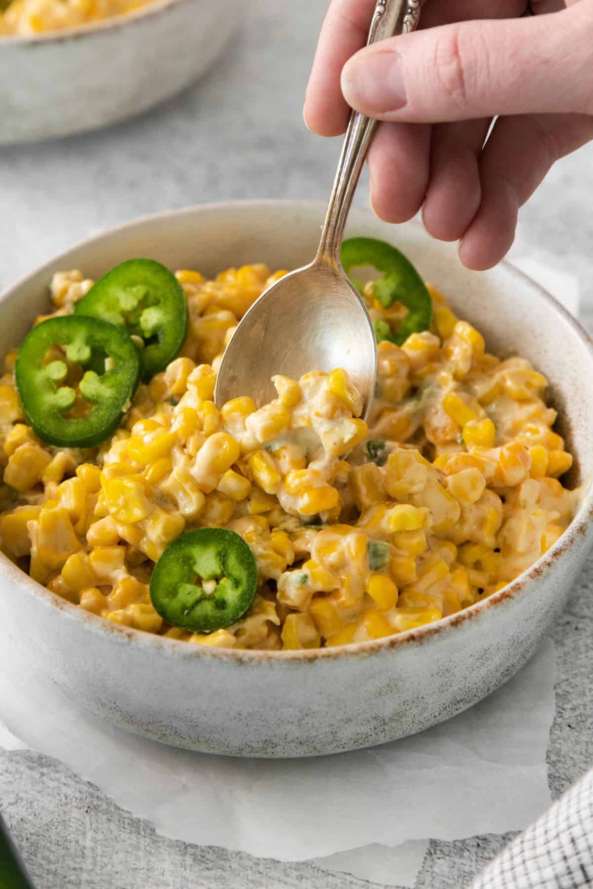 A spoon scooping out some jalapeno cream corn from a white bowl.
