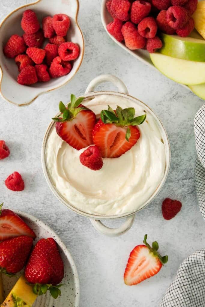 A bowl of marshmallow dip for fruit topped with strawberries.