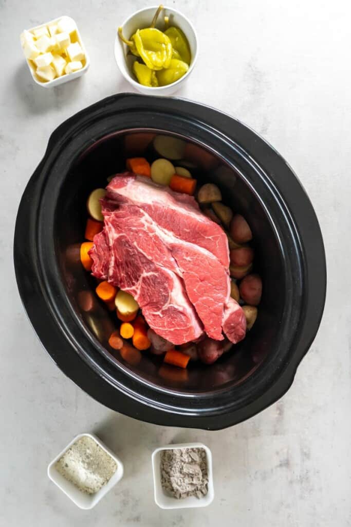Placing pot roast on top of vegetables in a black slow cooker.