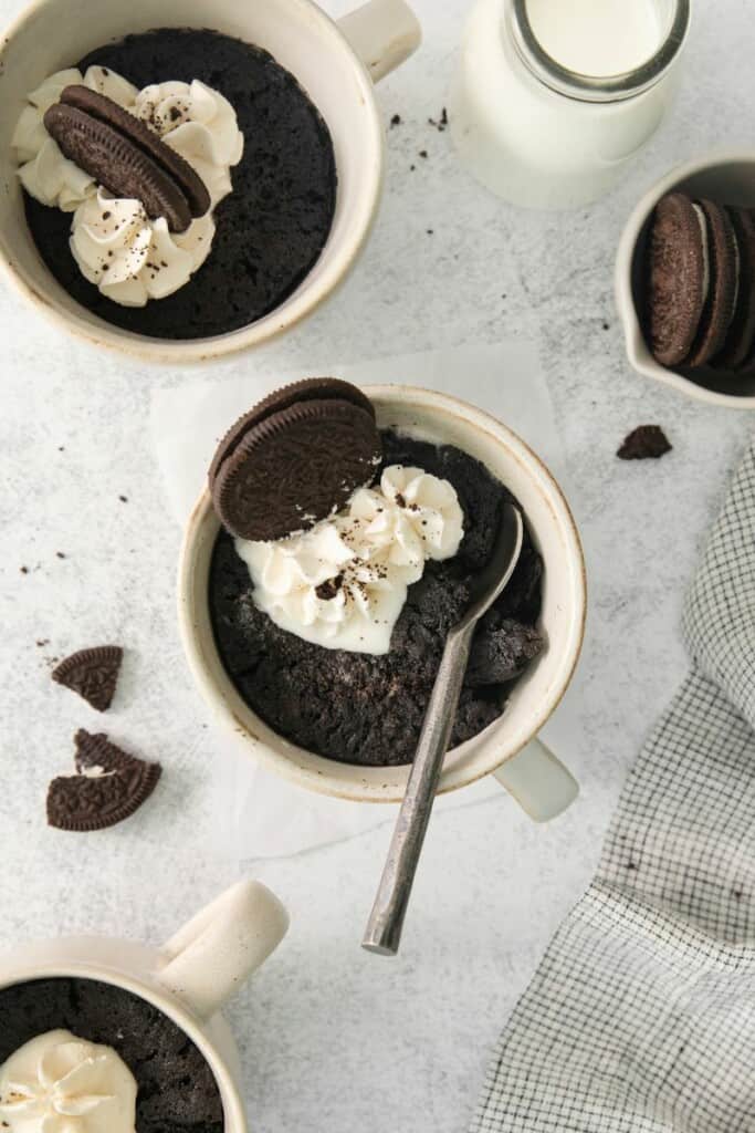 A spoon inside an oreo cake in a mug topped with whipped cream and whole oreos.