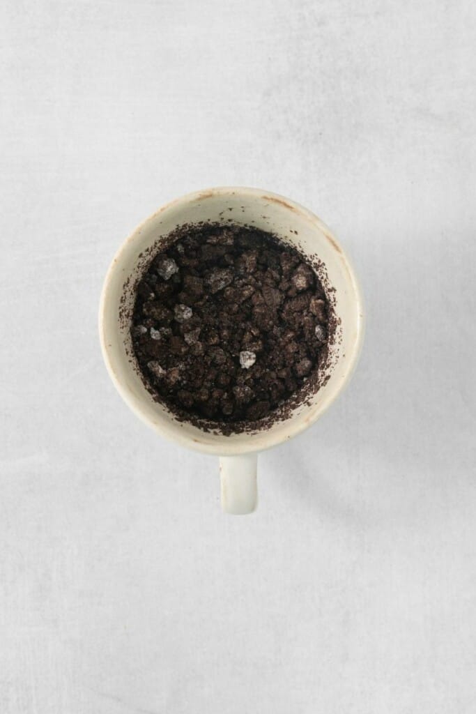 Adding milk and baking powder to crushed oreos in a mug.