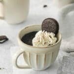 A prepared oreo cake in a mug topped with whipped cream and an oreo.