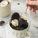 A fork lifting a bite of oreo cake out of a mug.