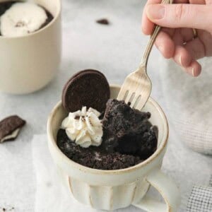 A fork lifting a bite of oreo cake out of a mug.