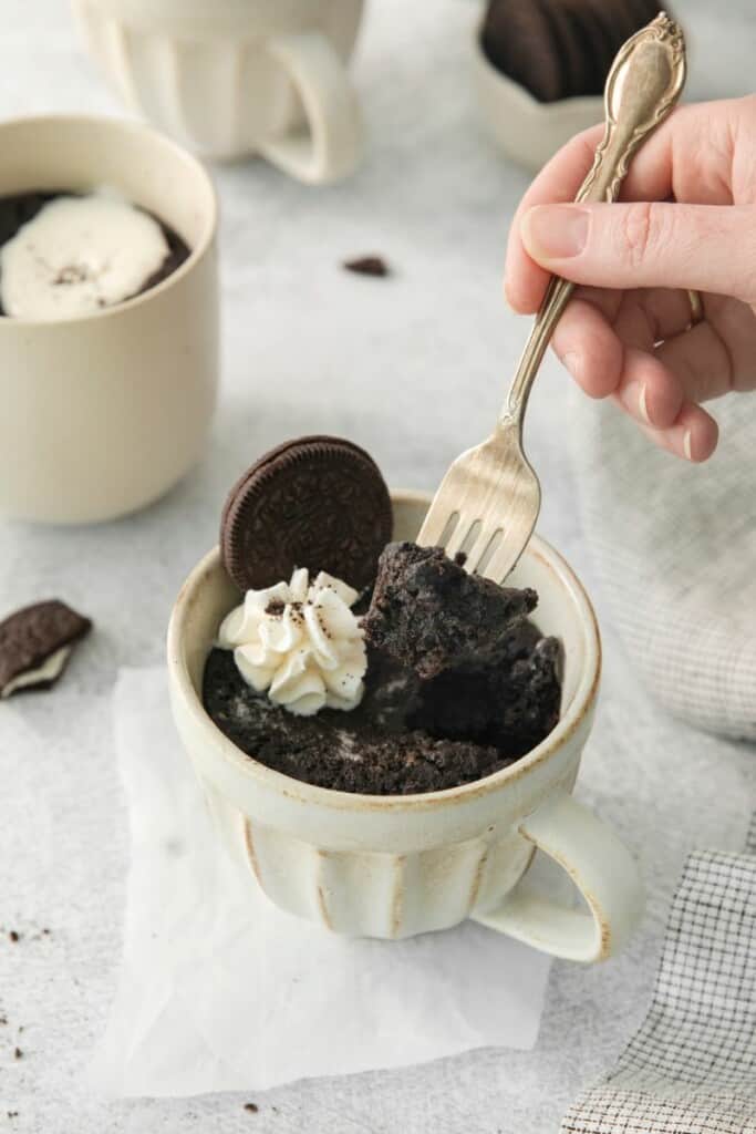 A fork lifting a bite of oreo cake out of a mug.