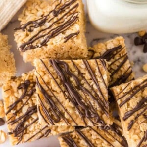 Rice Krispie Treat Squares made with peanut butter and chocolate drizzle with a glass of milk.