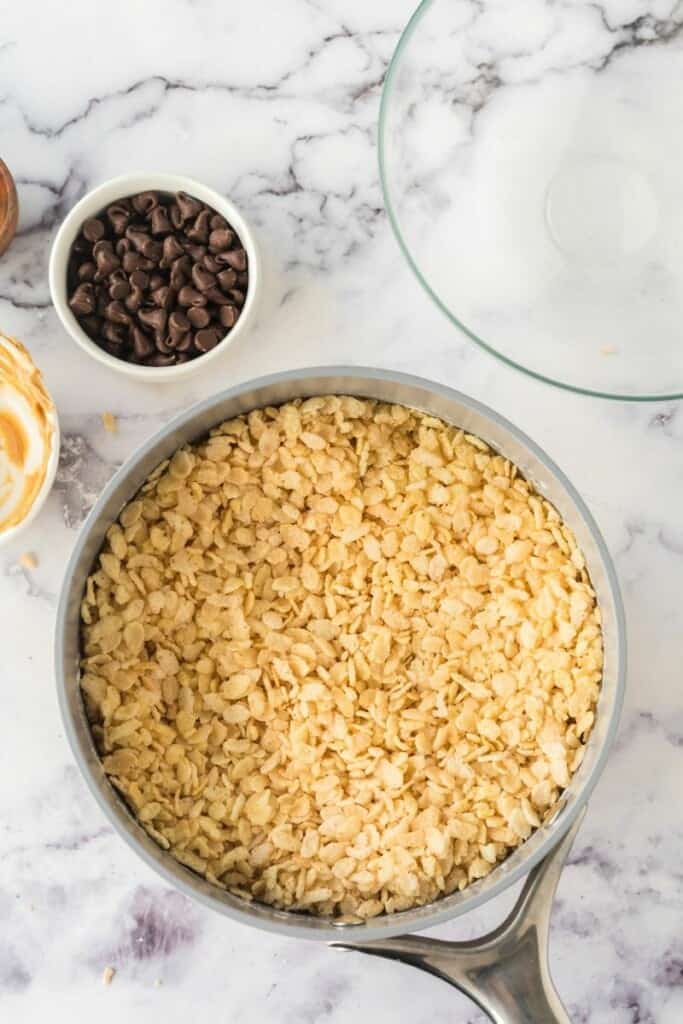 Adding rice krispies to peanut butter, marshmallow, and butter mixture in saucepan.