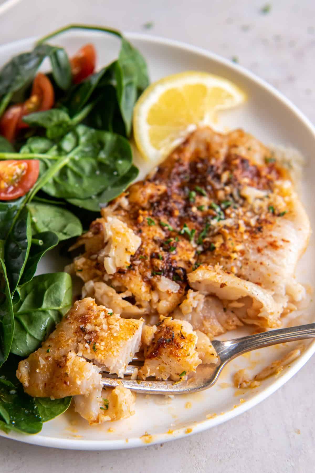 Close up of the air fryer flounder on a plate cut up a little bit so you can see the flakiness of the fish.
