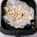 Popped popcorn in the air fryer basket with foil underneath.