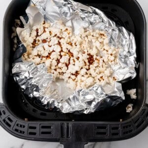 Popped popcorn in the air fryer basket with foil underneath.