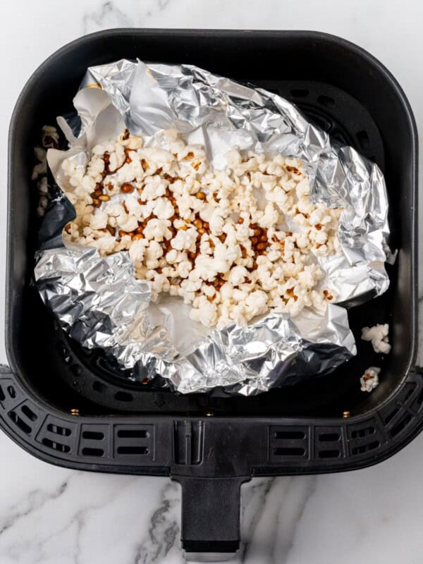 Popped popcorn in the air fryer basket with foil underneath.