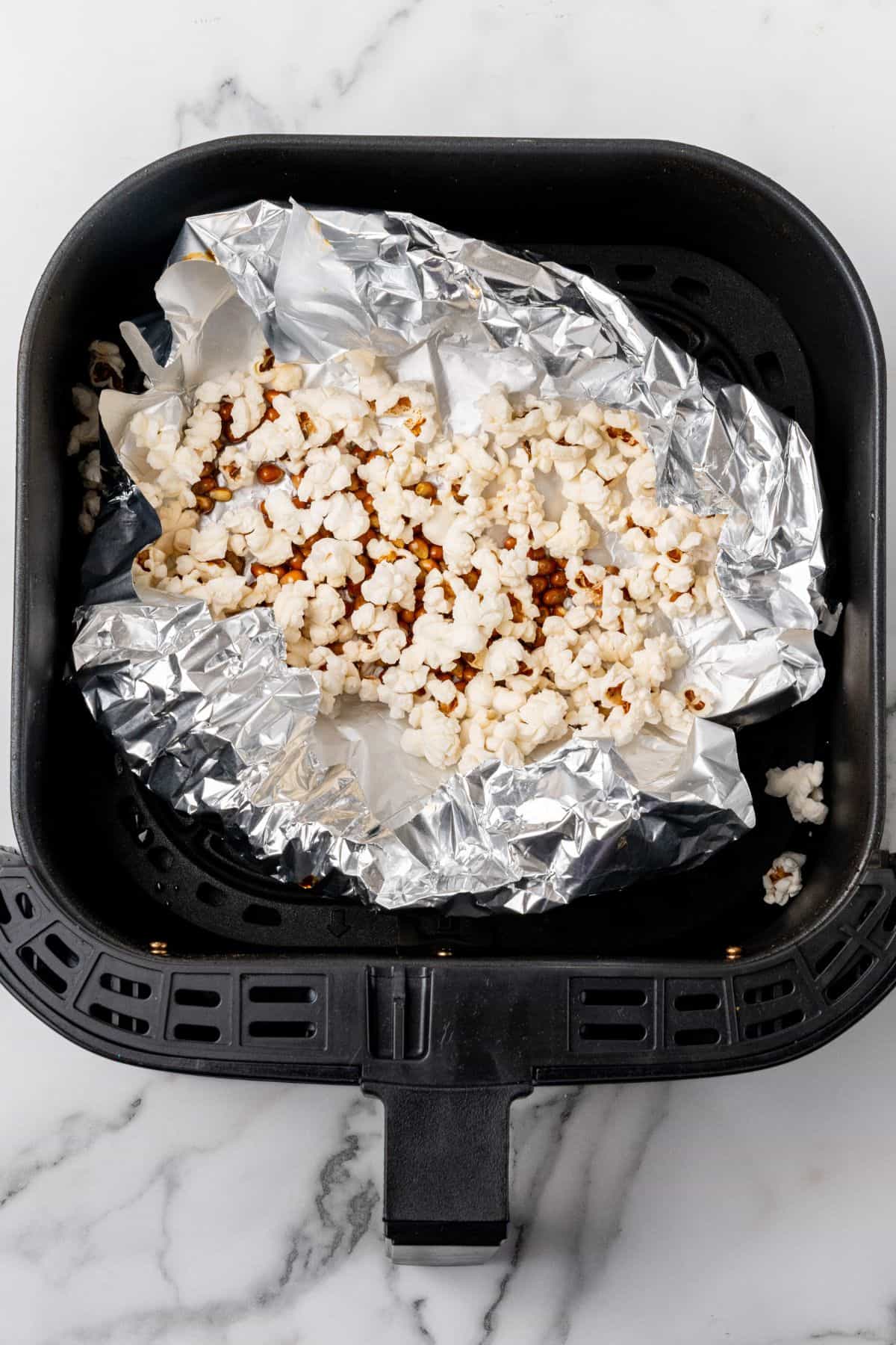 Popped popcorn in the air fryer basket with foil underneath.