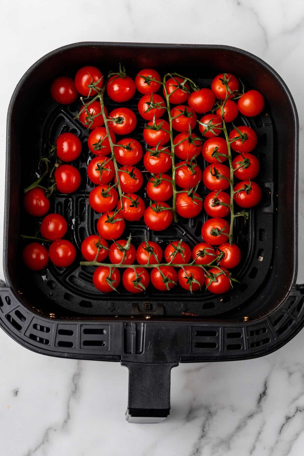 Raw cherry tomatoes on vines inside an air fryer basket.