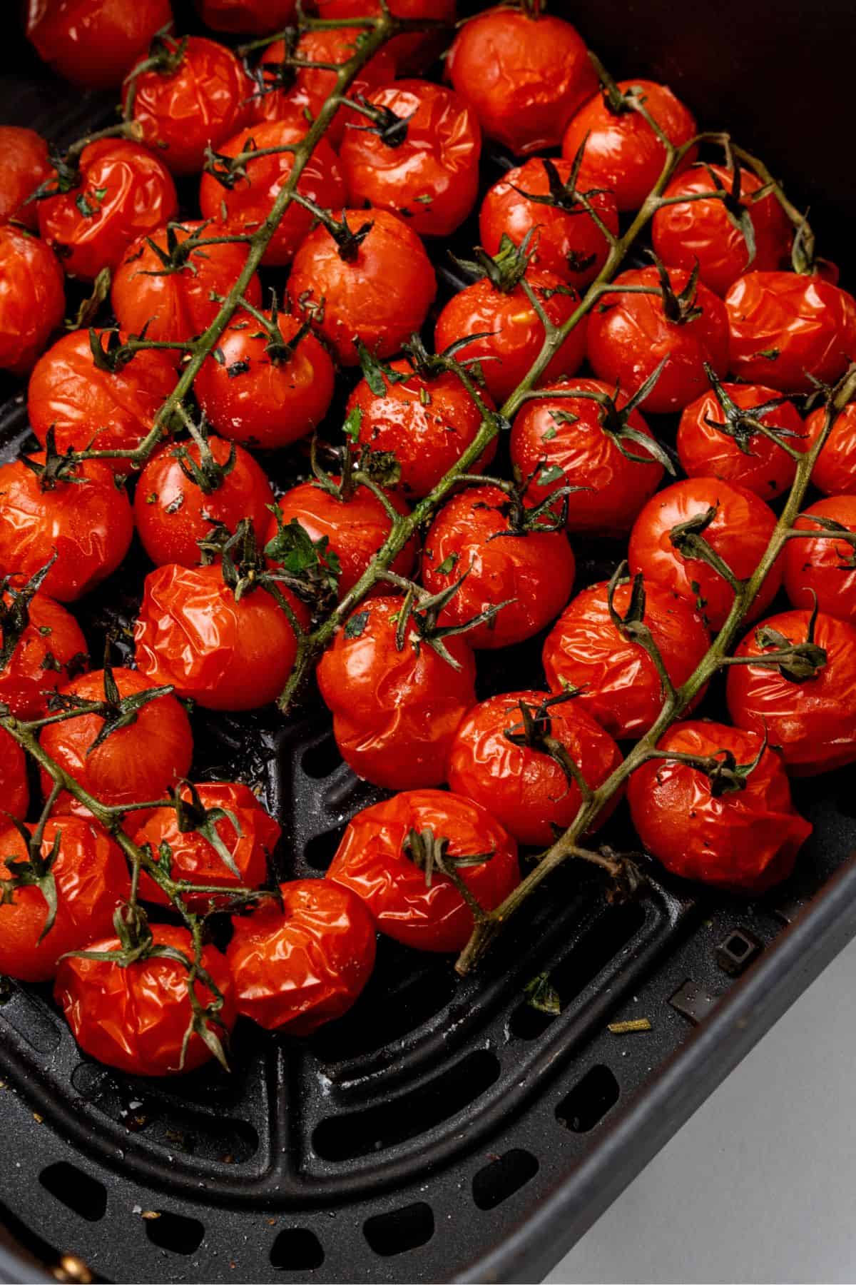 Close up of roasted tomatoes in an air fryer basket.